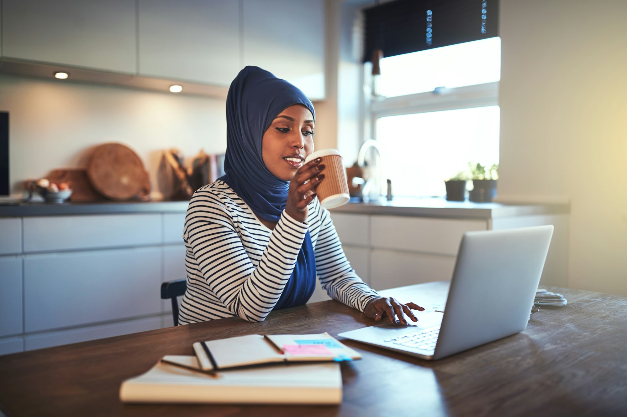 Young Arabic entrepreneur drinking coffee while working in her kitchen